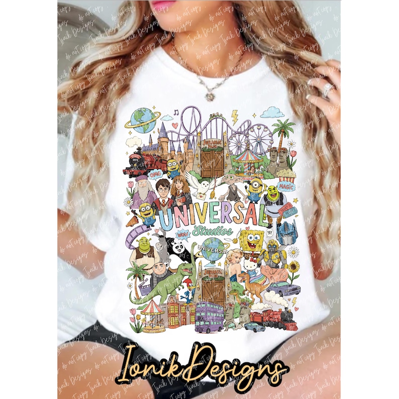 Puede incluir: Una camiseta blanca con un estampado gr&aacute;fico colorido de varios personajes animados, atracciones de parques tem&aacute;ticos y el texto Universal Studios. El dise&ntilde;o incluye ilustraciones de un globo terr&aacute;queo, monta&ntilde;as rusas y un castillo.