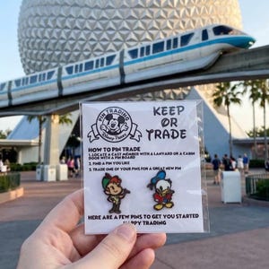 May include: A clear plastic card featuring two Disney character pins, Peter Pan and Donald Duck. The card includes the text Pin Trading, Keep or Trade, and instructions on how to trade pins with cast members at Disney Parks to get started.