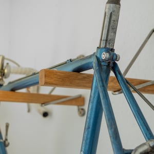 Könnte beinhalten: Ein blauer Fahrradrahmen ist an einem Wandregal aus Holz montiert. Das Regal ist mit Metallhalterungen an der Wand befestigt. Das Fahrrad hängt kopfüber.