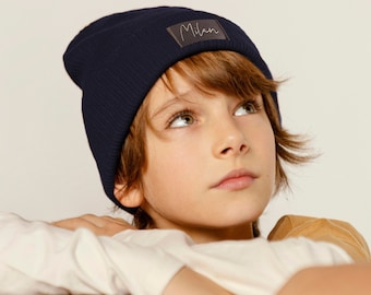 May include: A young person wearing a navy blue beanie with a black label that says "Milan" on it. The person is looking up and has brown hair.
