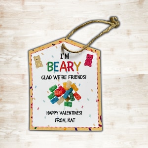 May include: A Valentine's Day gift tag with a house-shaped design. The tag features the text "I'M BEARY GLAD WE'RE FRIENDS!" and "HAPPY VALENTINES! FROM, KAT." Colorful gummy bears and confetti decorate the tag, which has a jute string for hanging.