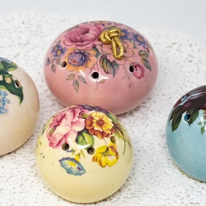 May include: Six ceramic ornaments with floral designs and gold string hangers. The ornaments are in various colours, including pink, blue, and cream.
