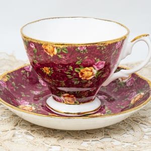 Peut inclure: Service à thé vintage composé d'une tasse et d'une soucoupe. La tasse et la soucoupe sont bordeaux avec un motif floral jaune et rose. Les bords sont dorés. La tasse a un intérieur blanc et une anse incurvée.