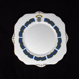 Peut inclure: Une assiette en céramique blanche avec une bordure dorée et un motif écossais bleu et vert. Au centre de l'assiette se trouve un blason avec un oiseau et une bannière qui dit "The Royal Scots".