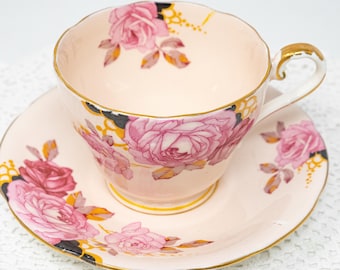 May include: A vintage teacup and saucer set. The pale pink cup and saucer are adorned with pink rose floral patterns and gold trim. The cup has a curved handle and a scalloped rim. The saucer also has a scalloped edge.