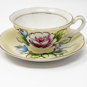 May include: A yellow teacup and saucer set with a floral design. The cup and saucer are decorated with a pink rose and green leaves.