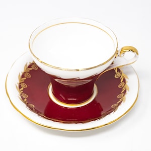 Peut inclure: Une tasse à thé blanche avec des bordures dorées et une soucoupe bordeaux avec des motifs floraux dorés. La tasse à thé a un intérieur bordeaux.