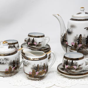 Peut inclure: Service à thé en porcelaine blanche avec un décor de paysage. L'ensemble comprend une théière, une crémière, un sucrier, des tasses et des soucoupes. Le paysage représente des arbres, des montagnes et un lac, avec des bordures dorées.