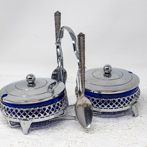Peut inclure: Un ensemble sucrier et crémier en argent avec des doublures en verre bleu et des cuillères assorties. L'ensemble est posé sur une nappe en dentelle blanche.