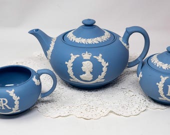 May include: A blue teapot, creamer, and sugar bowl set with white floral and crown designs. The teapot has a profile of a woman with a crown on her head. All three pieces have the letters "ER" on them.