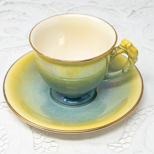 May include: A blue and yellow teacup and saucer set with a gold rim. The teacup has a unique handle shaped like a flower.