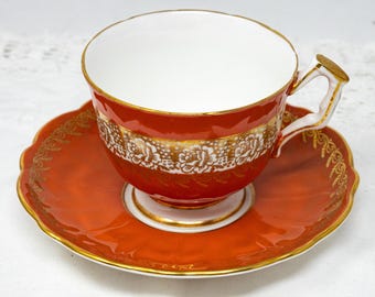May include: A vintage teacup and saucer set in a vibrant orange color with a white and gold floral design.