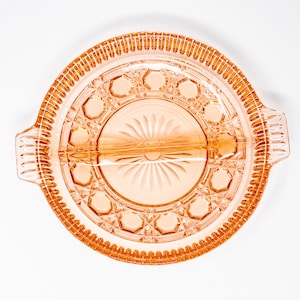 May include: A pink glass divided serving dish with a decorative pattern. The dish has a raised rim and a centre section with a starburst design.