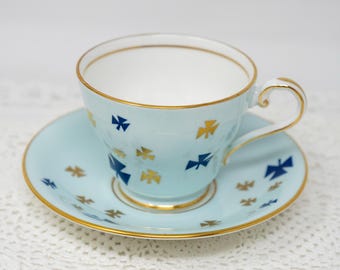 May include: A light blue teacup and saucer set with a gold rim and a pattern of blue and gold butterflies.