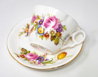 May include: A white teacup and saucer set with a floral pattern. The cup and saucer are decorated with pink, yellow, blue, and purple flowers. The cup has a gold rim and a handle.
