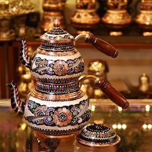 May include: A traditional Turkish tea set with a copper teapot decorated with colorful floral patterns. The teapot has two tiers and a wooden handle. The lid is also decorated with floral patterns.
