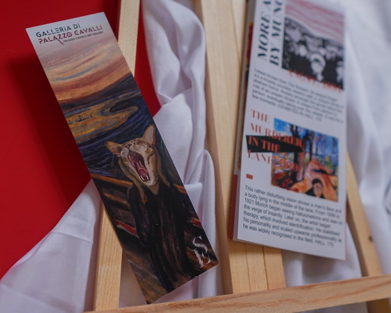 May include: A bookmark featuring a cat with an open mouth, a parody of Edvard Munch's "The Scream". The bookmark is on a wooden easel with a white cloth background. The text on the bookmark reads "Galleria di Palazzo Cavalli".