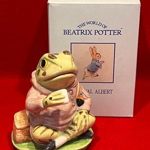 May include: A ceramic figurine of Mr. Toad from The Wind in the Willows by Beatrix Potter. The figurine is painted in shades of green, brown, and pink. Mr. Toad is wearing a pink jacket and holding a fishing rod. The figurine is sitting on a green base with a basket.