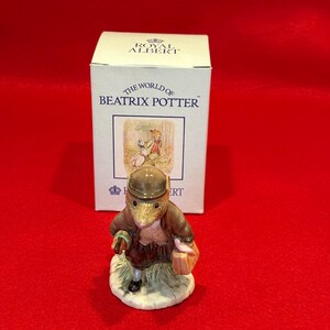 May include: A Royal Albert figurine of a mouse character from the Beatrix Potter series, wearing a brown hat and jacket, carrying a basket and a walking stick. The figurine is in front of its original box.