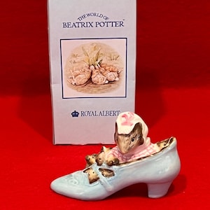 May include: A ceramic figurine of a mouse in a light blue shoe, wearing a pink and white checkered dress and a pink bonnet. The figurine is from the "World of Beatrix Potter" collection, with a matching box.