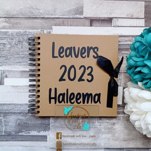 May include: A brown scrapbook with a black ribbon and the text "Leavers 2023 Haleema" on the front cover. The scrapbook is decorated with turquoise glitter.