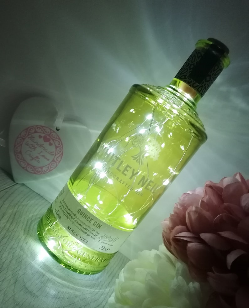 May include: A clear glass bottle with a green tint, filled with white fairy lights. The bottle is labelled "Whitley Neill Handcrafted Gin Quince Gin" and "Since 1762".