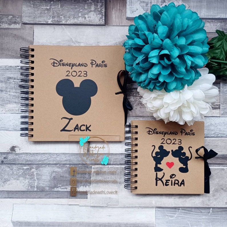 May include: Two brown scrapbook photo albums with black spiral binding. The covers are decorated with black Mickey Mouse silhouettes and the text "Disneyland Paris 2023". One album has the name "Zack" and the other has the name "Keira".