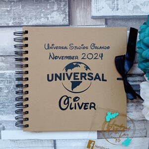 May include: A brown scrapbook with a black spiral binding. The cover has the text "Universal Studios Orlando November 2024" and a black globe with the word "Universal" in white text. The name "Oliver" is written in black cursive below the globe. A black ribbon is tied around the book.