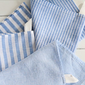May include: Four blue and white striped kitchen towels with white ties. The towels are folded and stacked on a white surface.