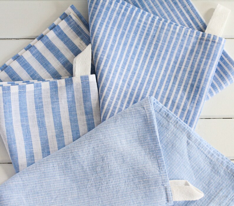 May include: Four blue and white striped kitchen towels with white ties. The towels are folded and stacked on a white surface.