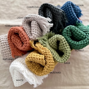 May include: A collection of waffle weave towels in various colors, including white, natural, terracotta, light gray, charcoal, ocean, forest, sage, mustard. The towels are rolled up and arranged in a circle.