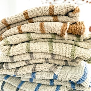 May include: A stack of four striped throw blankets in various colors, including brown, green, blue, and gray. The blankets are made of a soft, textured fabric and are folded neatly.