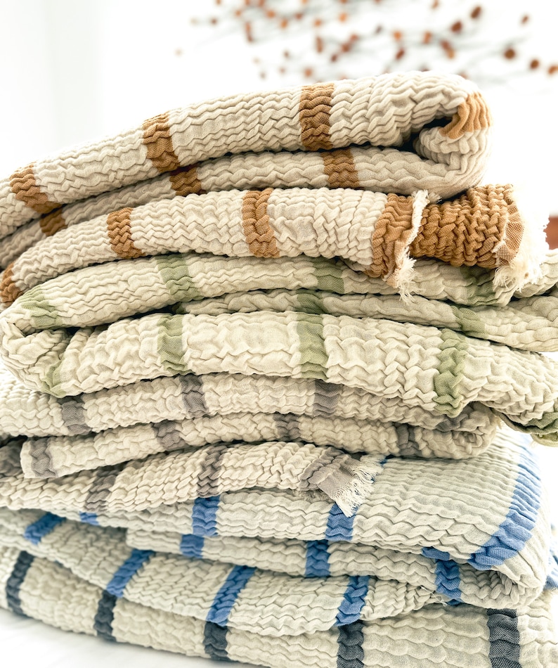 May include: A stack of four striped throw blankets in various colors, including brown, green, blue, and gray. The blankets are made of a soft, textured fabric and are folded neatly.