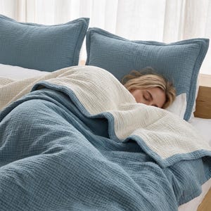May include: A bedding set featuring two blue pillow shams and a reversible blanket with a textured, crinkled fabric finish. The blanket displays a deep blue color on one side and a contrasting off-white color on the other, creating a layered look.