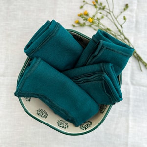 May include: A set of teal blue linen napkins folded and arranged in a white bowl with a green rim and a floral pattern.