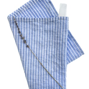 May include: A blue and white striped kitchen towel with a lavender sprig on top. The towel has a white loop sewn on the top corner.