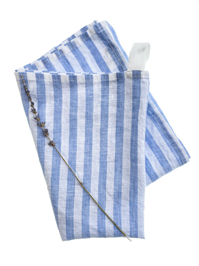 May include: A blue and white striped linen kitchen towel with a loop handle and a sprig of lavender.