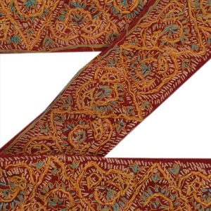 Peut inclure: Un ruban en tissu rouge foncé orné de broderies complexes en fil jaune doré et bleu clair. Le motif se compose de fleurs et de feuilles répétitives disposées en une séquence continue sur toute la longueur de la bordure textile.
