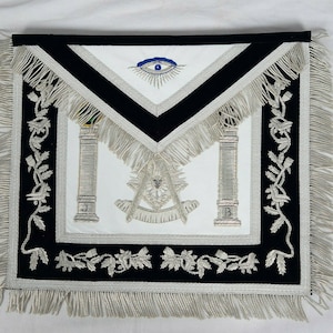 May include: A white Masonic apron with black velvet trim and silver fringe. The apron features an all-seeing eye, two pillars, and a compass and square.