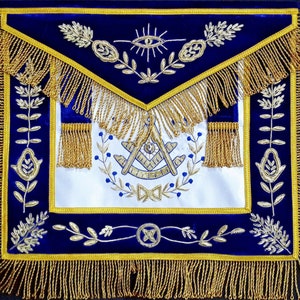 以下が含まれることがあります： 金色のフリンジと銀色の刺繍が施された青いフリーメイソンのエプロン。エプロンには、定規とコンパス、全能の目、花柄のデザインが施されています。