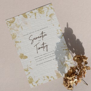 May include: A wedding invitation with a gold floral design on a white background. The invitation reads "You are invited to the wedding of Samantha and Timothy, Tuesday the twenty-fifth of July twenty-twenty at one o'clock in the afternoon, The Sunset Restaurant, Malibu."