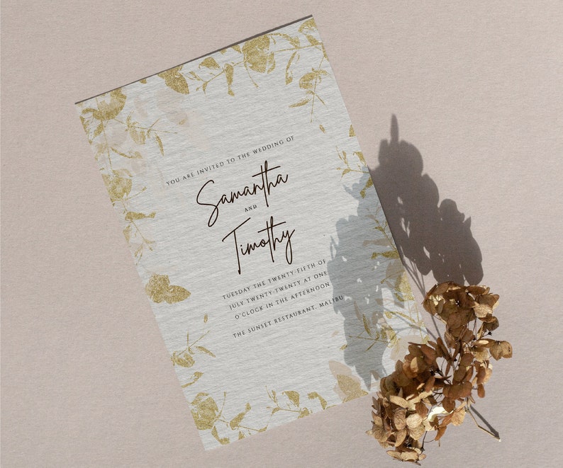 May include: A wedding invitation with a gold floral design on a white background. The invitation reads "You are invited to the wedding of Samantha and Timothy, Tuesday the twenty-fifth of July twenty-twenty at one o'clock in the afternoon, The Sunset Restaurant, Malibu."