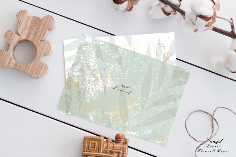 May include: A white card with a green and gold leaf pattern. The card has the word "Laurel" written on it in black script.