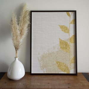 May include: A framed canvas print with a gold leaf design of a branch with leaves on a white background.
