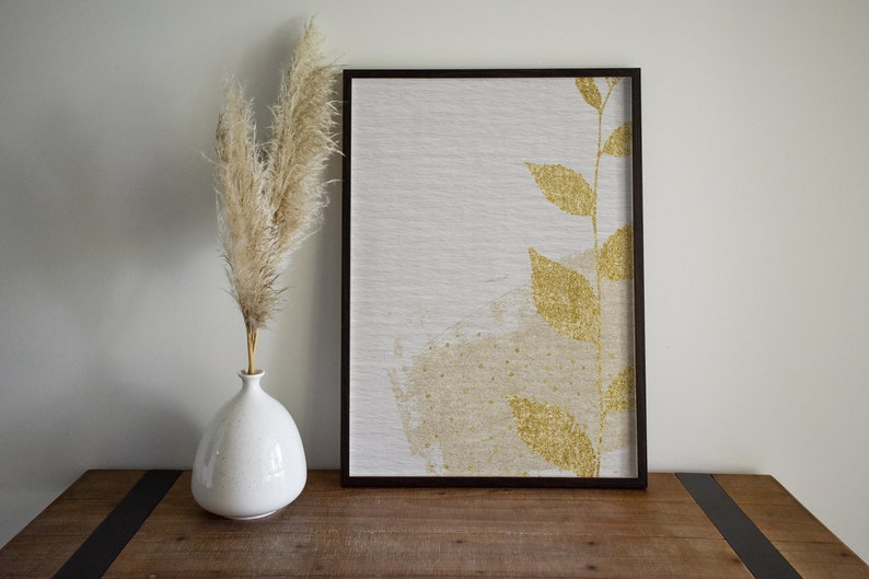 May include: A framed canvas print with a gold leaf design of a branch with leaves on a white background.