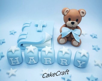 May include: Blue and white cake topper with a teddy bear holding a blue bow, a blue book with a cross on the cover, and the name "HARRY" spelled out in blue blocks.