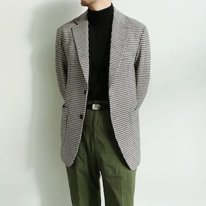 Könnte beinhalten: Ein Blazer mit schwarz-weißem Hahnentrittmuster, einem schwarzen Rollkragenpullover und einer olivgrünen Hose.