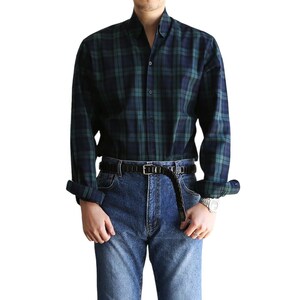May include: A long-sleeved plaid shirt in dark blue and green with a button-down collar. The shirt is worn with a black belt and blue jeans.