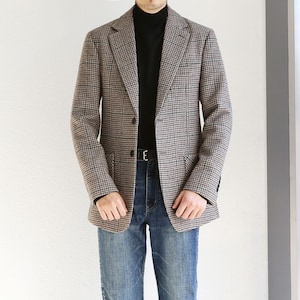 May include: A brown and black plaid blazer with a black mock neck shirt and blue jeans.