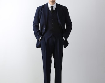 May include: A navy blue suit with a matching vest and a white dress shirt with a black tie. The suit has a classic fit and is tailored for a sharp look.